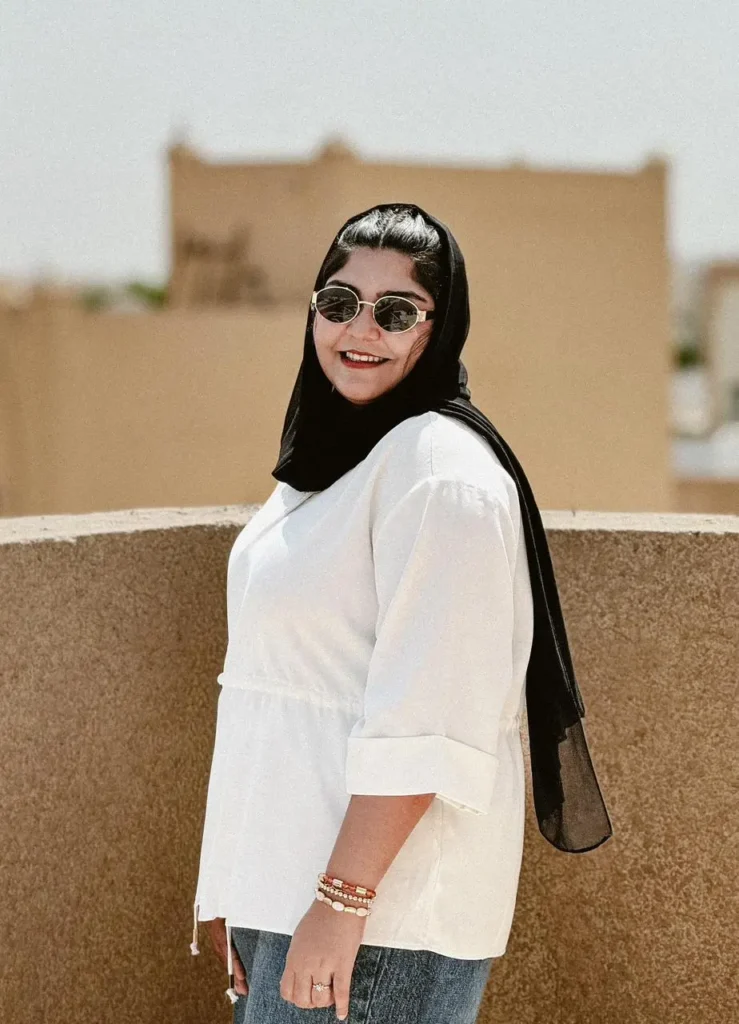 Professional portrait of a digital marketing specialist wearing a black hijab, smiling outdoors in a bright, modern setting.